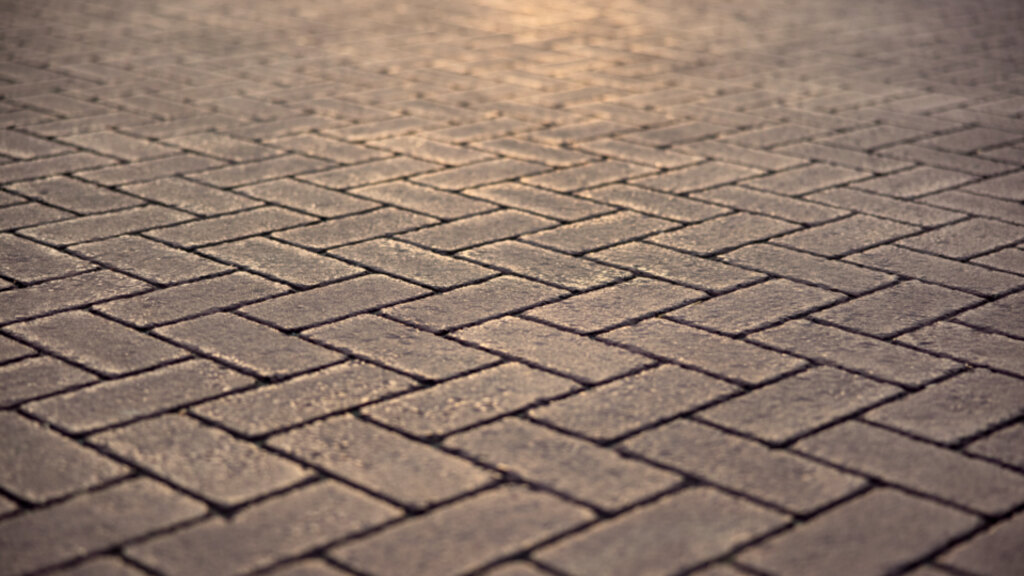Rectangular block pavers laid in a herringbone pattern, seen close up so the joints between the blocks run diagonally across the frame